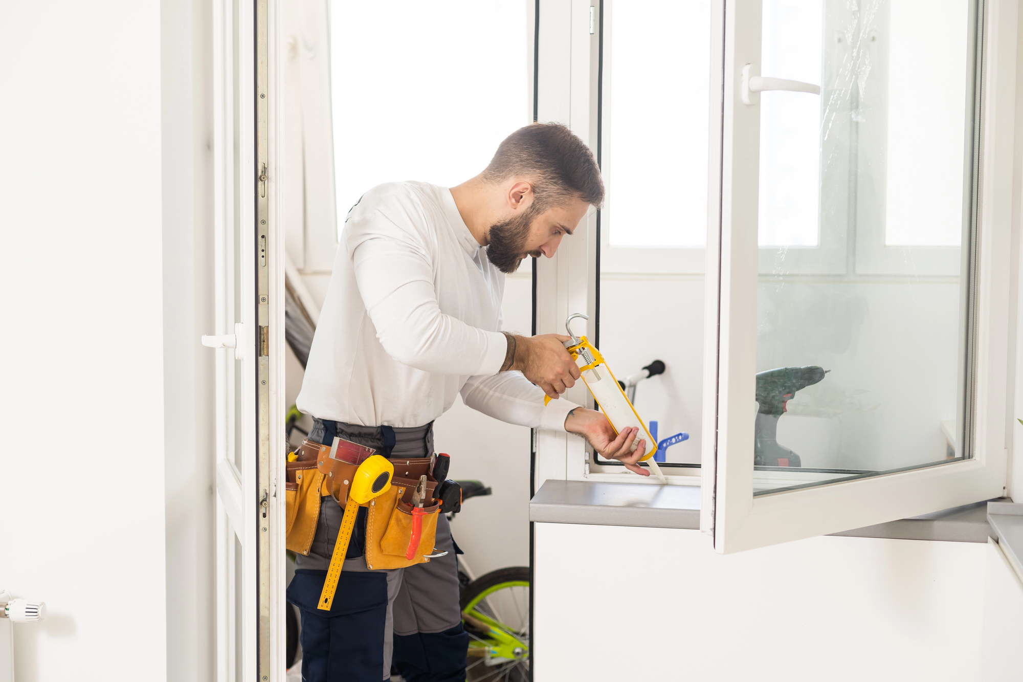 Hombre aplicando pegamento en una tabla al lado de una ventana